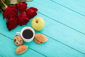 taza de café con croissants y galletas y rosas rojas sobre fondo de madera azul. copie el espacio Bosquejo. vista superior. día de la madre de san valentín. foto