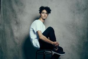 cute guy with curly hair sitting on a chair studio photo