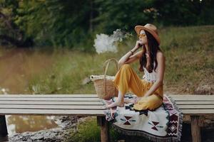 Woman in hippie clothes sitting in nature by the lake on a bridge relaxing and admiring the scenery photo