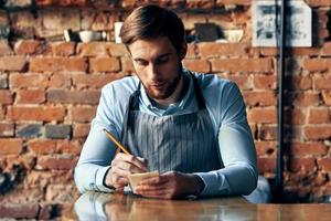 a man in an apron sits at a table accepting an order a cafe waiter photo