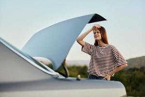 un mujer tristemente mira dentro el abierto maletero de un coche durante un detener en el la carretera en el camino a naturaleza. foto