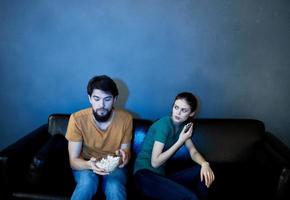 Emotional woman and man on the couch with popcorn watching TV photo