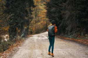 happy traveler with backpack walks on the road in autumn forest photo