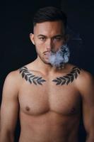 Modelling snapshots. Pensive serious tanned attractive handsome naked man thinking looks at camera to you smoking posing isolated in black studio background. Fashion offer. Copy space for ad. Closeup photo