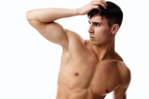 confident man athlete with a pumped-up torso touches his head with his hand on a light background photo