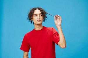 Pensive thoughtful unhappy young curly tanned Caucasian guy in basic red t-shirt posing isolated on over blue background. Lifestyle and Emotions concept. Good offer with copy space for ad photo