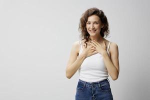 Overjoyed shocked surprised happy curly beautiful woman in basic white t-shirt fold hands on chest posing isolated on over white background. People Emotions Lifestyle concept. Copy space photo