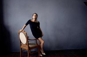 beautiful woman in a black dress near the chair luxury fashion dark background photo