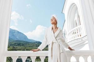 Portrait of gorgeous woman in a white robe on the balcony bit on green nature Lifestyle photo