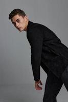 A man in a dark suit on a gray background leaned to the side for a cropped view photo