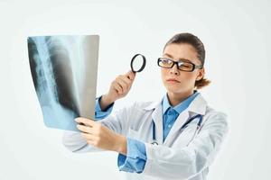 a nurse in a white coat looks through a magnifying glass at an x-ray photo