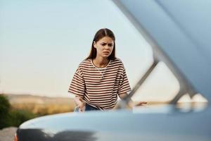 The young woman driver looks at the car in horror by opening the hood. A car broke down on a road trip photo