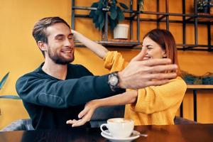 joven personas en amor abrazando mientras sentado a un mesa en un café y naranja pared interior foto