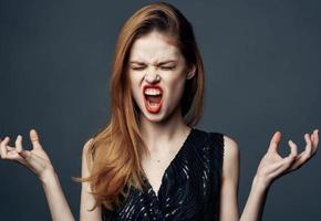 retrato de emocional mujer en un negro vestir en un gris antecedentes con brillante maquillaje y oscuridad en el párpados foto