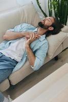 A man with a beard sleeps on the couch in the afternoon tired and relaxed after stress and ill health. Stress at work, poor sleep and health problems photo