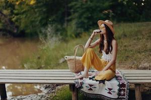 Woman in hippie clothes sitting in nature by the lake on a bridge relaxing and admiring the scenery photo