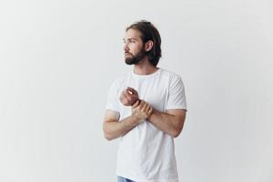 Portrait of a man with a black thick beard and long hair in a white T-shirt on a white isolated background emotion of sadness and longing photo