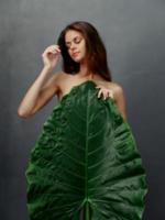 pretty woman with large green leaf covers naked body dark background photo