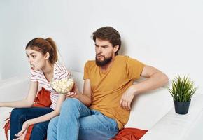 A man and a woman on the couch watching TV with popcorn in a plate photo