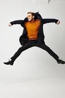 man jumped up with legs and arms spread wide orange sweater model photo