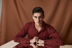 A man on a cloth background with folds sits at a table with a mirror photo