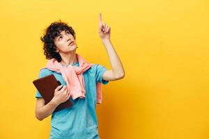 student in a blue T-shirt with a notepad yellow background photo