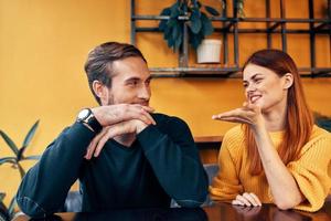 alegre hombre y mujer gesticulando con su manos y sentado a un mesa en un café comunicación amigos un taza de café foto