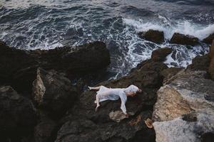 woman in long white dress wet hair lying on a rocky cliff landscape photo