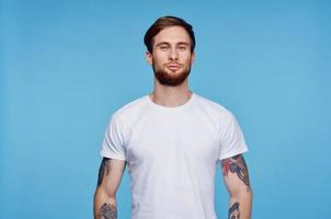 handsome man in white t-shirt tattoos on his arms cropped view blue background photo