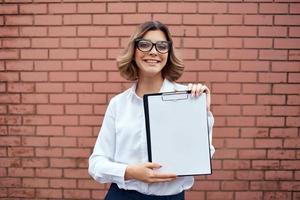 Business woman with folder for papers in hands outdoors near brick wall photo