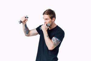 guy in a black t-shirt with dumbbells in his hands on a white background fitness pumped up muscles tattoo photo