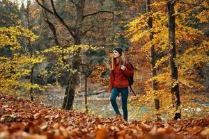 mujer turista camina mediante el parque en otoño con un mochila en su espalda y alto arboles paisaje río lago foto