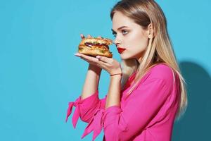 alegre rubia en un rosado camisa hamburguesa rápido comida bocadillo azul antecedentes foto