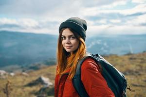 retrato de un viajero en un rojo chaqueta y sombrero y con un mochila al aire libre en el montañas Fresco aire foto