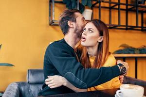 young people in love hugging while sitting at a table in a cafe and orange wall interior photo