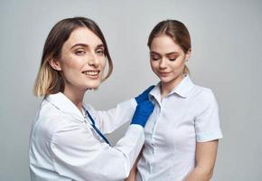 Happy woman doctor in blue gloves and female patient in white t-shirt stethoscope medical gown photo