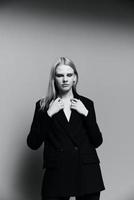A stylish lady in a suit keeps her hands on the collar and puts on a jacket in the studio. The concept for the new collection. Classic black and white photo