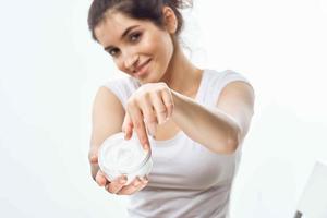 cheerful brunette in a white t-shirt with a jar of cream in her hands skin care light background photo