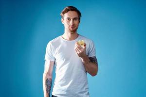 cute guy with a tattoo and in a white t-shirt on a blue background eating apples cropped view photo