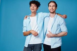 joven hombres en idéntico camisas abrazando en un azul antecedentes mejor amigos divertido foto