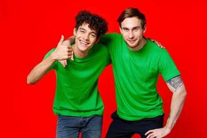 two friends in green t-shirts hugs fun red background photo