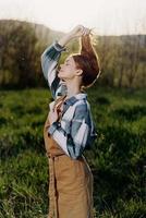 Young woman fixes her long red hair in nature in the sunset sunlight photo