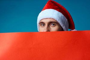 Cheerful man in a santa hat holding a banner holiday blue background photo