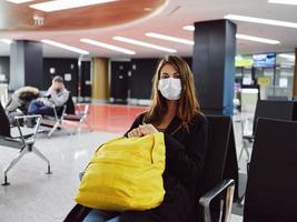 mujer pasajero vistiendo médico máscara a aeropuerto esperando amarillo mochila foto