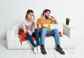cheerful man and woman on the couch with popcorn and red plaid flower in a pot emotions photo