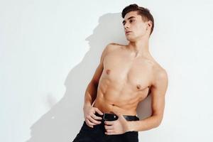 A sexy guy with a naked torso and in black trousers on a light background, a falling shadow photo