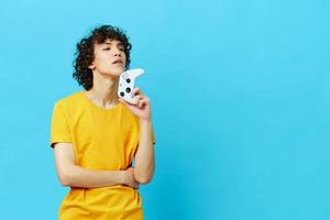 gamer plays with joystick in yellow t-shirts blue background photo