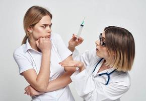 A nurse in a medical gown holds a syringe in her hand and a patient on a light background photo