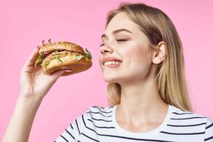 woman in striped t-shirt hamburger delicious sandwich snack pink background photo