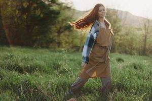 un mujer corriendo mediante un campo en un verano día con largo fluido pelo en el rayos de el ajuste Dom. el concepto de libertad y armonía con naturaleza foto